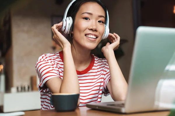 Retrato de mujer asiática complacida con auriculares usando el ordenador portátil en —  Fotos de Stock