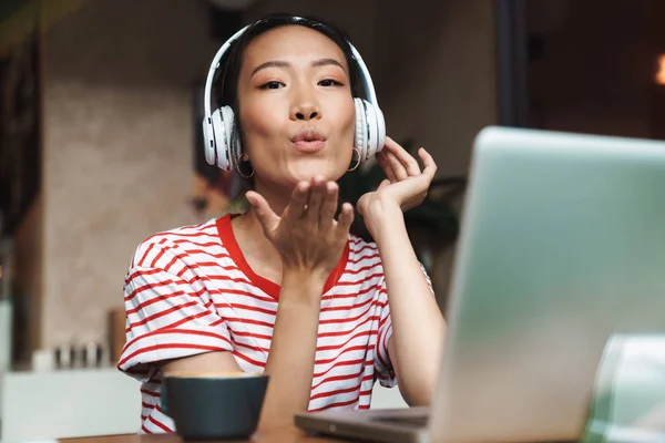 Retrato de mujer asiática con auriculares soplando aire beso en la cafetería —  Fotos de Stock