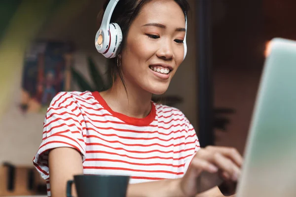 Retrato de mujer asiática encantadora con auriculares usando el ordenador portátil en —  Fotos de Stock