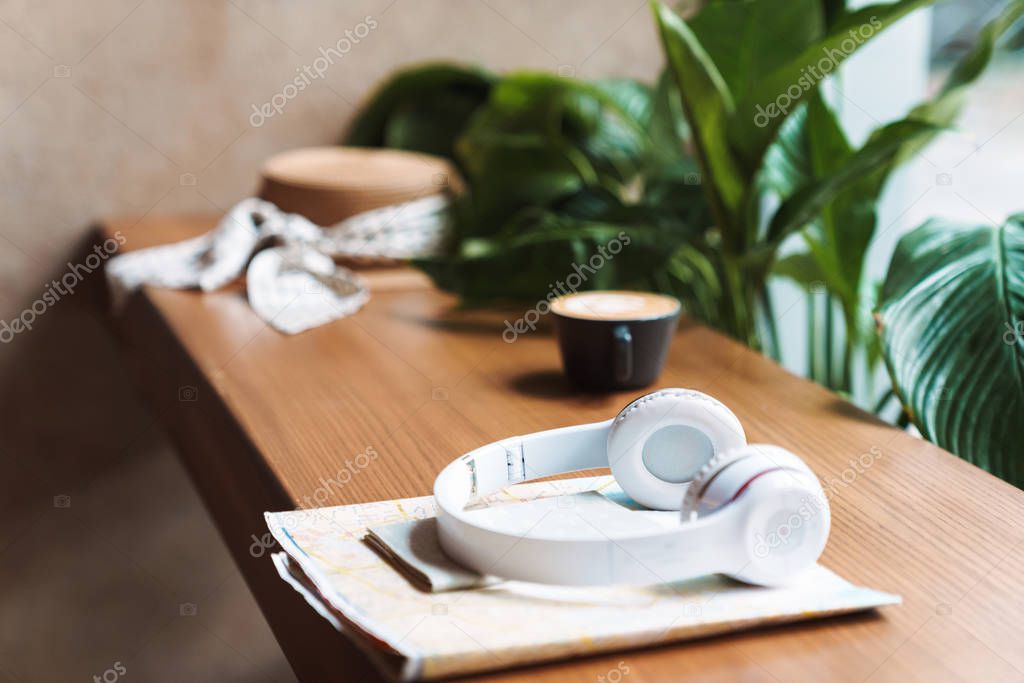 Image of cup of coffee, headphones, passport, paper map on woode