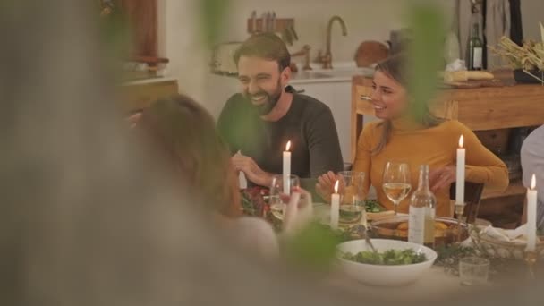 テーブル席で一緒にお祝いの家族のディナーで休んでいる幸せな素敵な大きな家族の葉のビューを通して — ストック動画
