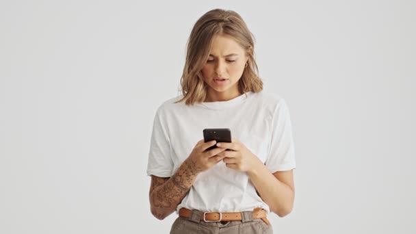 Δυσαρεστημένη Νεαρή Γυναίκα Που Φοράει Βασικό Μπλουζάκι Χρησιμοποιώντας Smartphone Της — Αρχείο Βίντεο