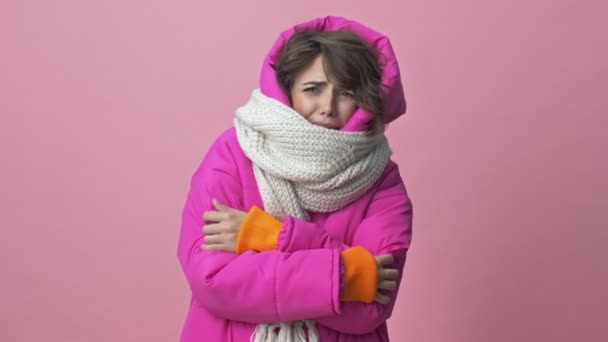 Nieszczęśliwa Młoda Kobieta Ubrana Zimową Kurtkę Szalikiem Zamarza Różowym Tle — Wideo stockowe