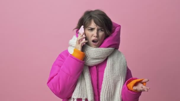 Angry young woman wearing a winter jacket with a scarf is screaming on her smartphone while having a call isolated over a pink background — Stock Footage Angry Young Woman Wearing Winter Jacket Scarf Screaming Her Smartphone Stock Footage
