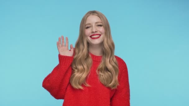 幸せなかなり女性でセーター挨拶誰かとトルコ石の背景の上にカメラを見て — ストック動画