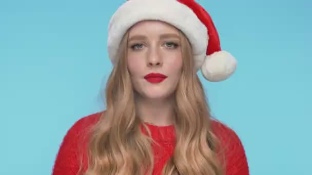 近看欢愉的神秘美女头戴圣诞礼帽 眼睛眨着 在蓝绿色的背景下看着相机 — 图库视频影像