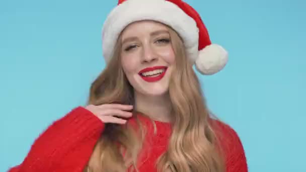 閉じるビューの再生可能な美しい女性でクリスマスの帽子遊びとともに彼女の髪とトルコ石の背景にカメラを見て — ストック動画