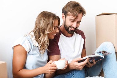 Otururken kahve içip dergi okuyan çiftin fotoğrafı.