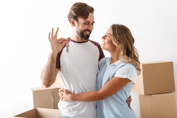 Photo of smiling couple hugging near cardboard boxes and holding keys — 스톡 사진