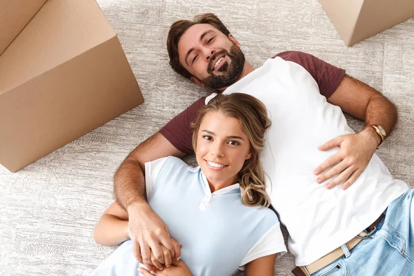 Photo of smiling couple looking at camera and lying near boxes — 스톡 사진