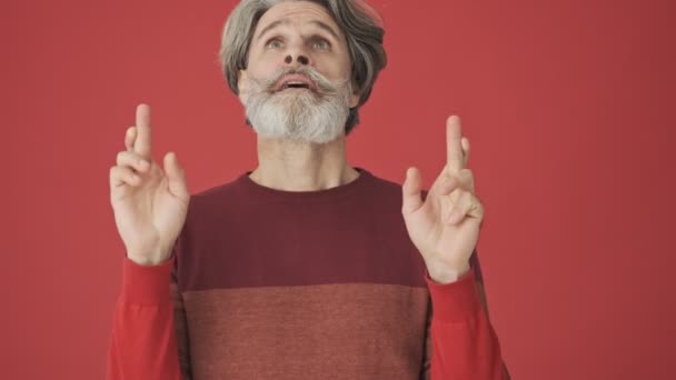 一位穿着红色毛衣的英俊的白发苍苍的大胡子老人在红墙上相互交叉着手指 保持着祈祷的姿势 — 图库视频影像