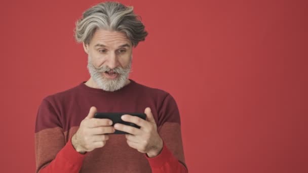 Happy Surprising Gray Haired Bearded Man Red Sweater Using Smartphone — ストック動画