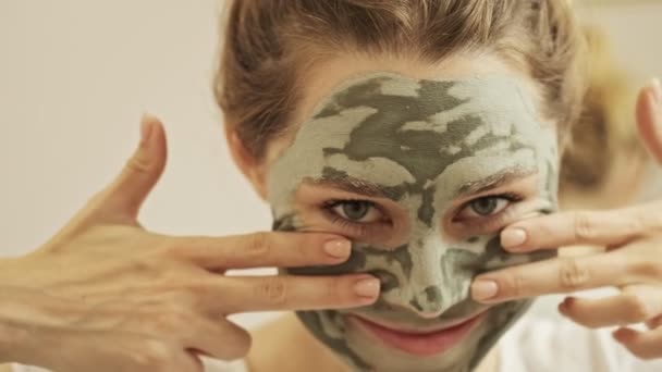 站在浴室里 脸上戴着绿色面具 脸上挂着滑稽表情的快乐年轻女子的近景 — 图库视频影像