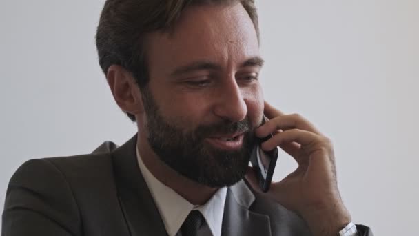 オフィスに座っている間にスマートフォンで話して幸せなハンサムな髭のビジネスマンのビューを閉じます — ストック動画