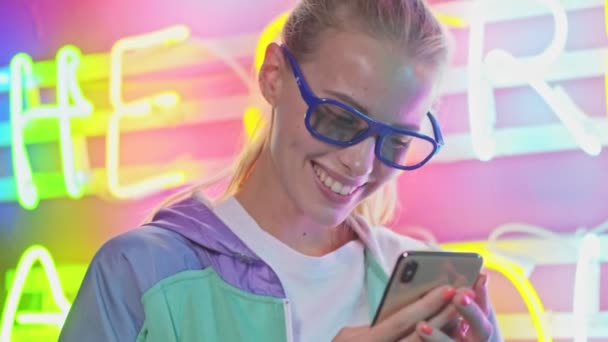 Güneş Gözlüklü Neşeli Genç Bayanın Renkli Neon Duvarın Üzerinde Akıllı — Stok video