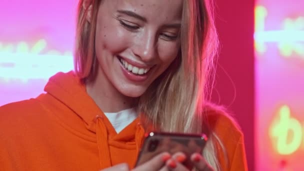 Close up view of happy young pretty woman using smartphone and enjoying over colorful neon wall — Stock Footage Close View Happy Young Pretty Woman Using Smartphone Enjoying Colorful — Stock Video