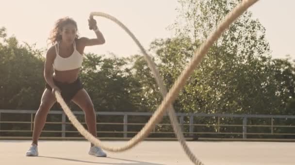 スポーツウェアを着たアフリカ系アメリカ人の強い女性が屋外の遊び場でロープで横断ツアーをしています — ストック動画
