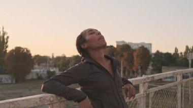 Sakin Afrikalı Amerikalı kadın spor giyim kuşamında eski köprü üzerinde çalışırken korkuluklara yaslanıyor.