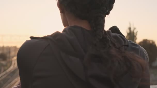 穿着运动服 头戴辫子的非洲裔美国女人的背景图 一边靠在栏杆上一边 一边在老桥上向太阳望去 — 图库视频影像