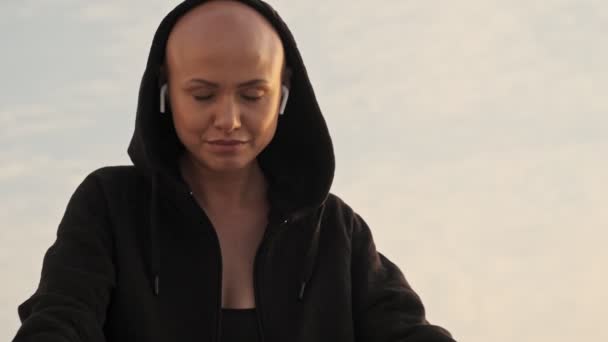 坐在耳机里欣赏音乐 在户外海边享受这一刻的迷人的秃头女运动员 — 图库视频影像