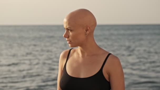 一个严肃而迷人的秃头女运动员站在室外海面上 把目光移开 — 图库视频影像