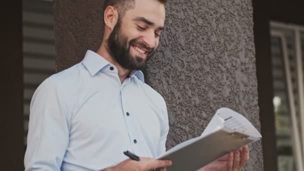 陽気な髭のビジネスマンがクリップボードに何かをチェックして書き 屋外で幸せになる — ストック動画