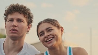 Kaygısız, mutlu, kıvırcık erkek tenisçiye yakından bakın. Tenis kortunda mutlu bayan rakibiyle birlikte dinleniyor.