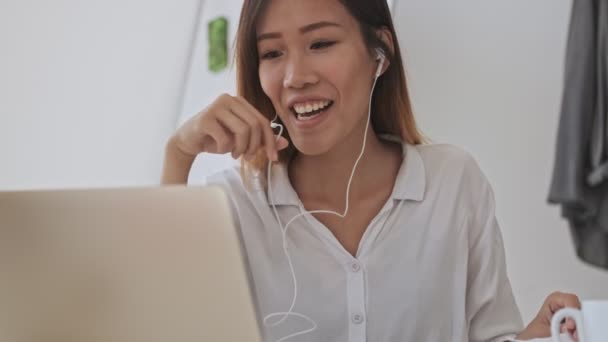 在办公室使用有线耳机打电话的同时 积极的亚洲商界女性也在使用笔记本电脑 — 图库视频影像