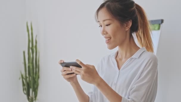 Uśmiechnięta Szczęśliwa Azjatycka Kobieta Pomocą Smartfona Trzymając Poziomo Białym Biurze — Wideo stockowe