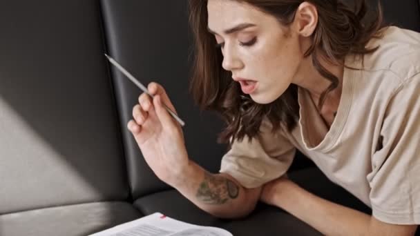 Concentrated Pretty Brunette Woman Studying Magazine While Lying Sofa Indoors — 비디오