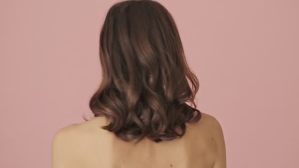 バックビューの半分裸の美しい女性はピンクの背景に隔離されたカメラに回っている — ストック動画