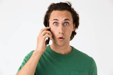 Basit tişörtler giyen esmer adamın şaşırmış görüntüsü. Akıllı telefonla konuşuyor.