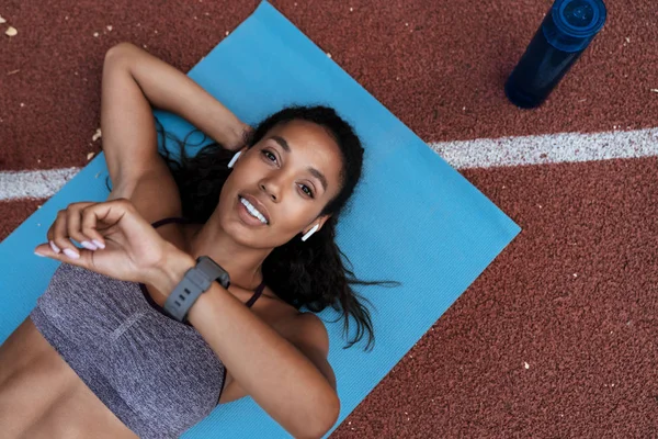 Imagen de una mujer afroamericana mirando un reloj de pulsera en la estera —  Fotos de Stock