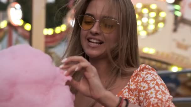 遊園地でピンク色の大きなお菓子を食べている魅力的な女性 — ストック動画