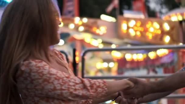 遊園地で手をつなぎながら笑顔の若い夫婦と女が渦巻く幸せ — ストック動画