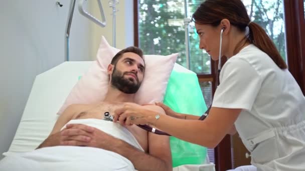 Femeie Doctor Uniformă Medicală Examinând Tânăr Pacient Stetoscop Apoi Zâmbind — Videoclip de stoc