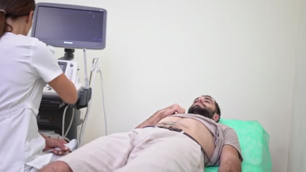 A young man is getting abdominal ultrasound scan by female doctor in medical uniform at hospital — Stock Footage Young Man Getting Abdominal Ultrasound Scan Female Doctor Medical Uniform Royalty Free Stock Footage