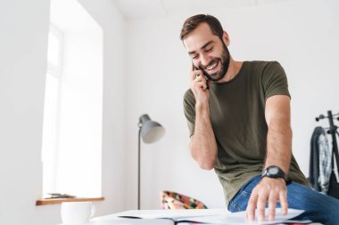 Cep telefonuyla konuşan ve dokümanları okuyan genç bir adamın görüntüsü