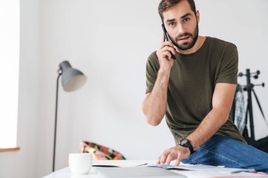Cep telefonuyla konuşan ve belgeleri okuyan genç bir adam resmi