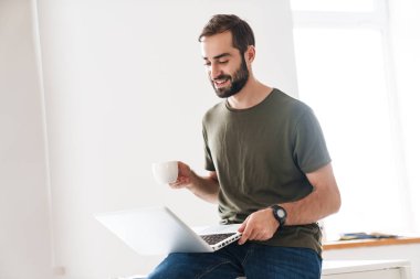 Laptopta yazan ve kahve içen yakışıklı bir adam resmi.