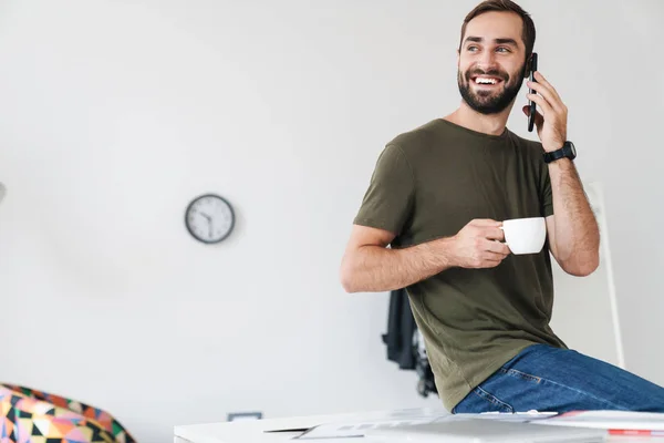 Bild eines kaukasischen fröhlichen Mannes, der mit dem Handy telefoniert und Kaffee trinkt — Stockfoto