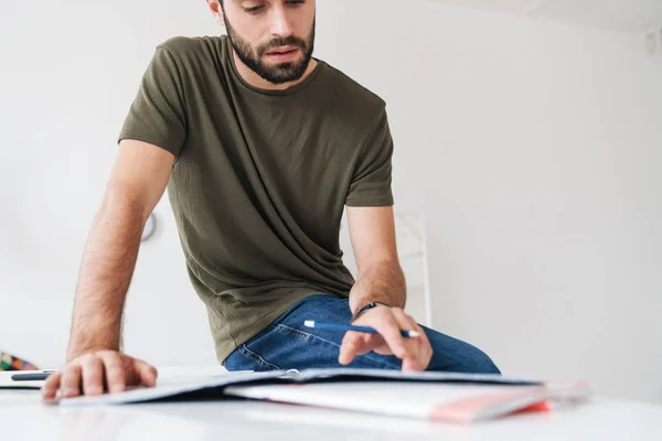 Image d'un jeune homme caucasien concentré lisant des documents et prenant des notes — Photo