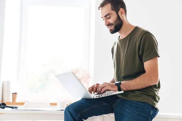 Imagen del hombre guapo enfocado escribiendo en el portátil y sonriendo — Foto de Stock