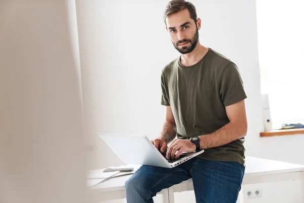 Bild eines gutaussehenden ernsten Mannes in lässigem T-Shirt, der auf Laptop tippt — Stockfoto