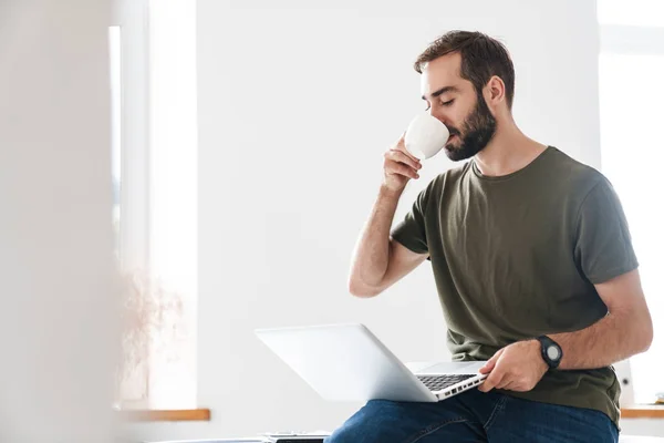 Bild eines gutaussehenden Mannes, der auf seinem Laptop tippt und Kaffee trinkt — Stockfoto