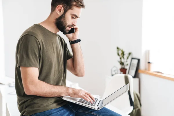 Bild eines gutaussehenden, ernsthaften Mannes, der mit Handy und Laptop spricht — Stockfoto