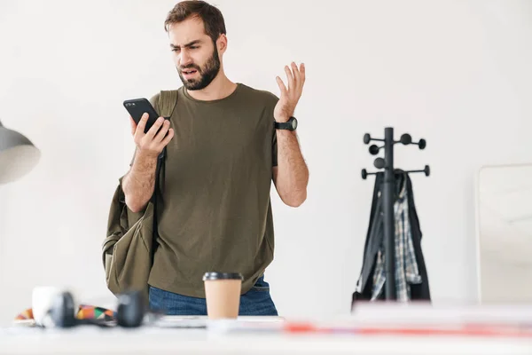 Imagen del hombre apuesto irritado sosteniendo y mirando el teléfono celular — Foto de Stock