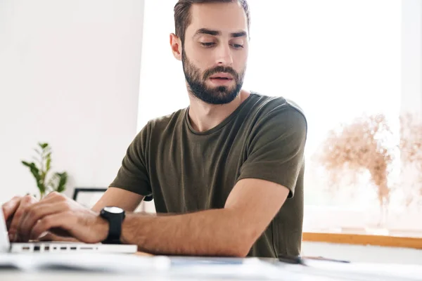 Immagine di bell'uomo pensante che digita su laptop e legge documenti — Foto Stock