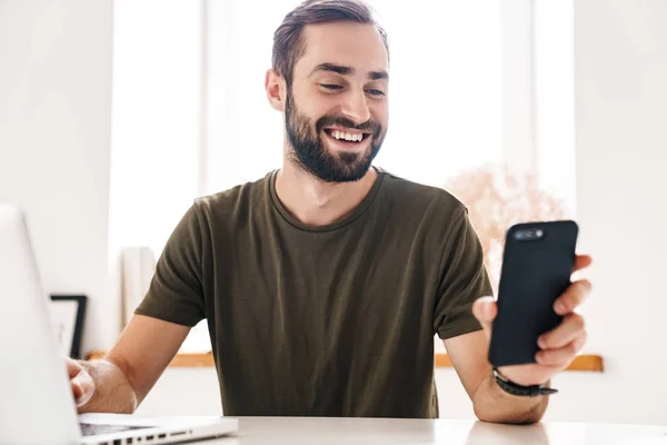 Image of handsome happy man typing on laptop and using cellphone — Stock Photo, Image
