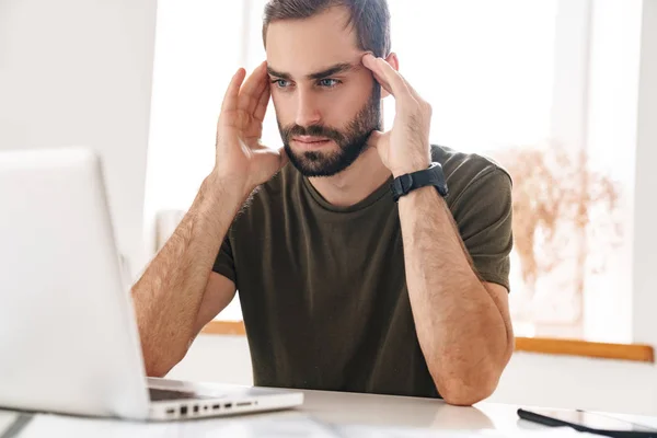 Imagen del hombre guapo enfocado mirando a la computadora portátil mientras está sentado —  Fotos de Stock